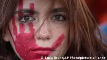 Mulher com marca vermelha de uma mão pintada no rosto em protesto contra a violência de gênero