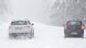Dois carros, um branco e um negro, trafegam em estrada coberta de neve Dois carros, um branco e um negro, trafegam em estrada coberta de neve