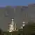 Die Türme und Kuppeln der Synagoge heben sich vor der Felswand des Tafelberg ab; im Vordergrund sind grüne Laubbäume zu sehen