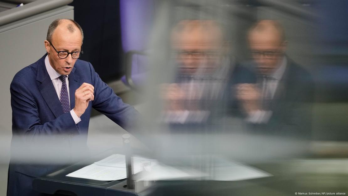 Friedrich Merz, Fraktionschef und CDU-Vorsitzender, steht im Bundestag am Rednerpult und hält eine Rede. Er trägt einen dunkelblauen Anzug, ein helles Hemd und eine Brille mit dunklem Gestell. Merz hat die rechte Hand erhoben und gestikuliert. 