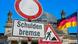 Verkehrsschilder Baustelle, Durchfahrt verboten, Wort "Schuldenbremse" vor dem Reichstagsgebäude und der deutschen Flagge