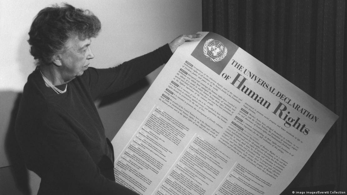 Eleanor Roosevelt segura grande papel com os artigos da Declaração.  Foto em preto e branco.