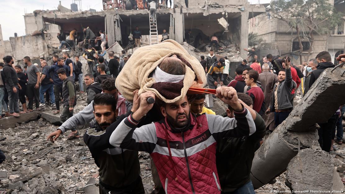 Homens carregam mulher doente em meio a escombros de um bombardeio