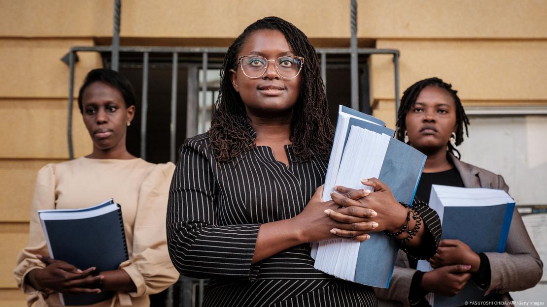 Mercy Mutemi, con carpetas en la mano, flanqueada por dos mujeres con carpetas. Mercy Mutemi, con carpetas en la mano, flanqueada por dos mujeres con carpetas.
