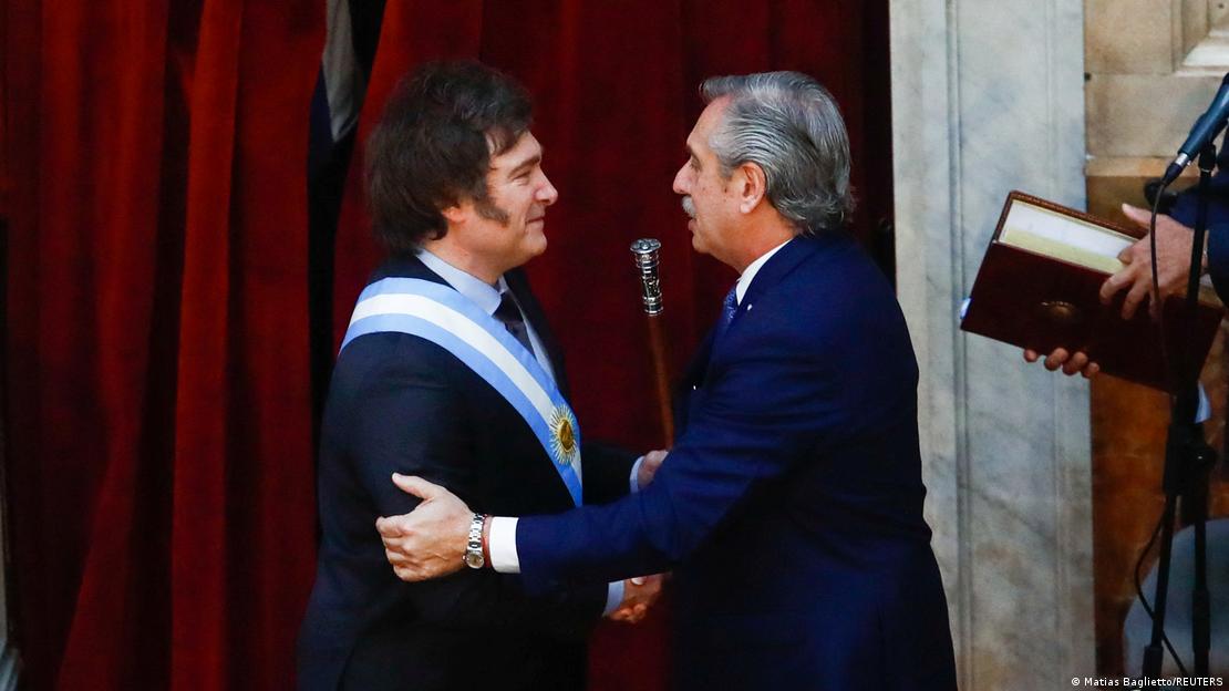 Milei com a faixa presidencial segura o bastão e cumprimenta Fernández