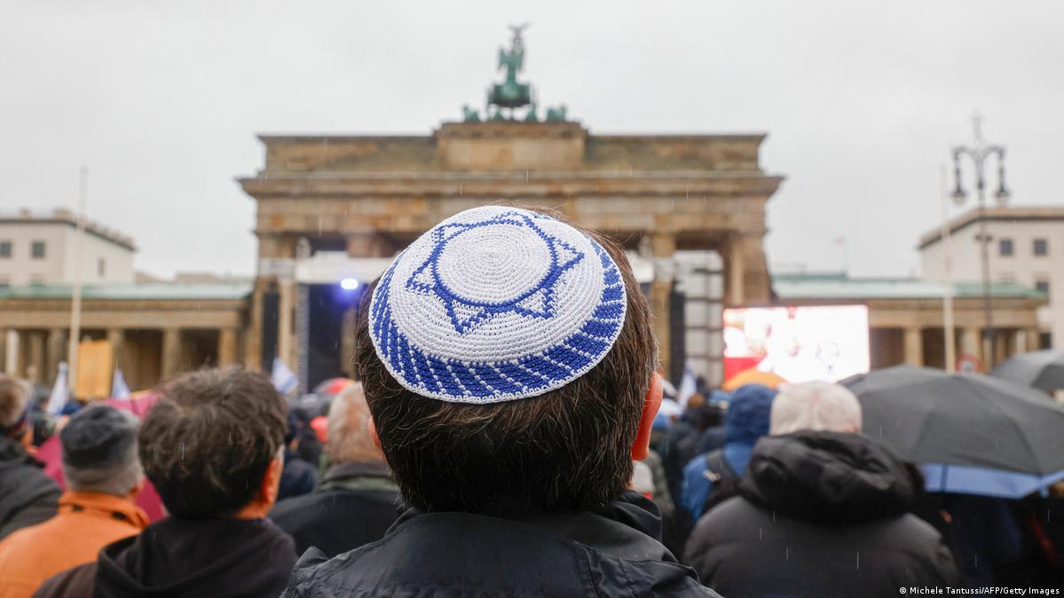 A man in a yarmaluke designed like the Israeli flag standing in  crowd at the Brandeburg Gate in Berlin
