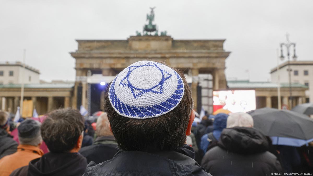 A man in a yarmaluke designed like the Israeli flag standing in  crowd at the Brandeburg Gate in Berlin