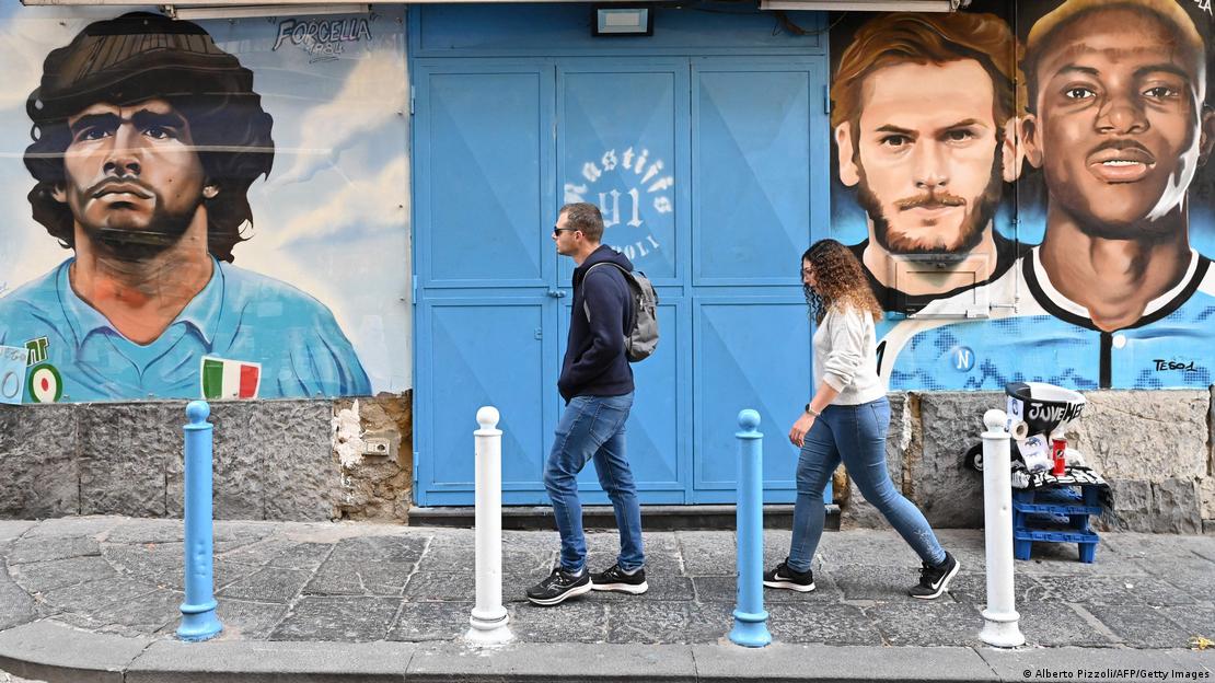 A man and a woman walk past murals of Napoli players Diego Maradona, Khvicha Kvaratskhelia and Victor Oshimhen A man and a woman walk past murals of Napoli players Diego Maradona, Khvicha Kvaratskhelia and Victor Oshimhen