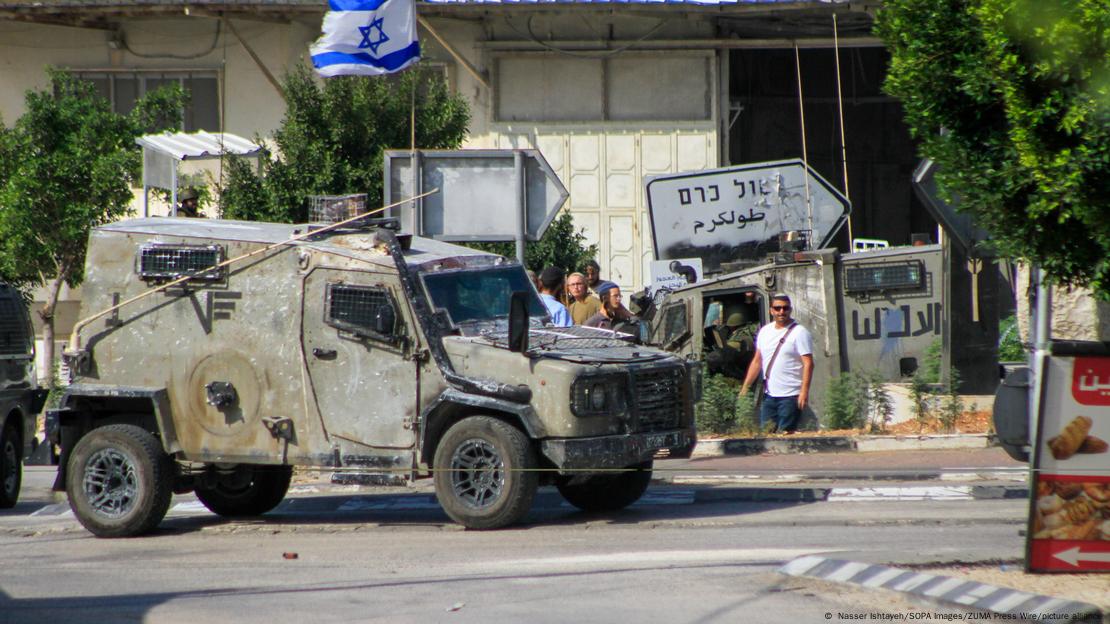 Ein Militärjeep mit israelischer Flagge; im Hintergrund ist ein auf Hebräisch und Arabisch beschriftetes Straßenschild zu sehen