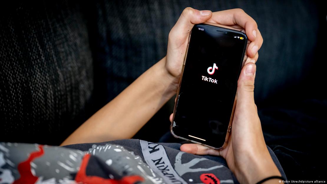 Dos manos sosteniendo un teléfono móvil con el logotipo de TikTok apareciendo en la pantalla.