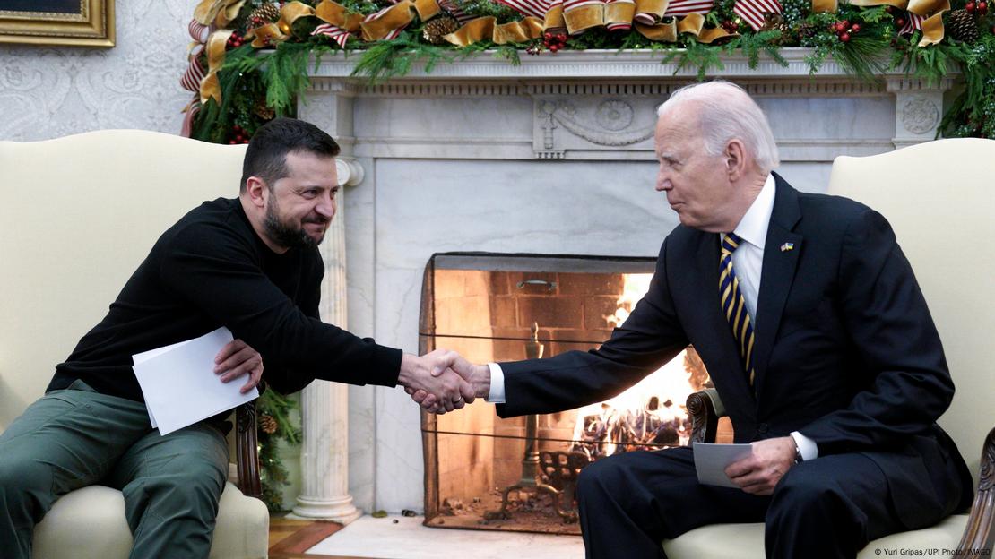 Der ukrainische Präsident Wolodymyr Selenskyj und US-Präsident Joe Biden sitzen nebeneinander in Sesseln und geben sich die Hand  