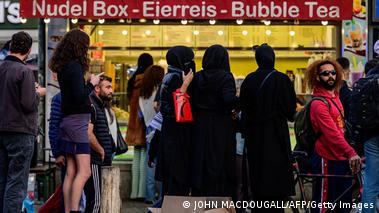 Three women wearing a Niqab stand in front of a food stand at Berlin's Hermannplatz