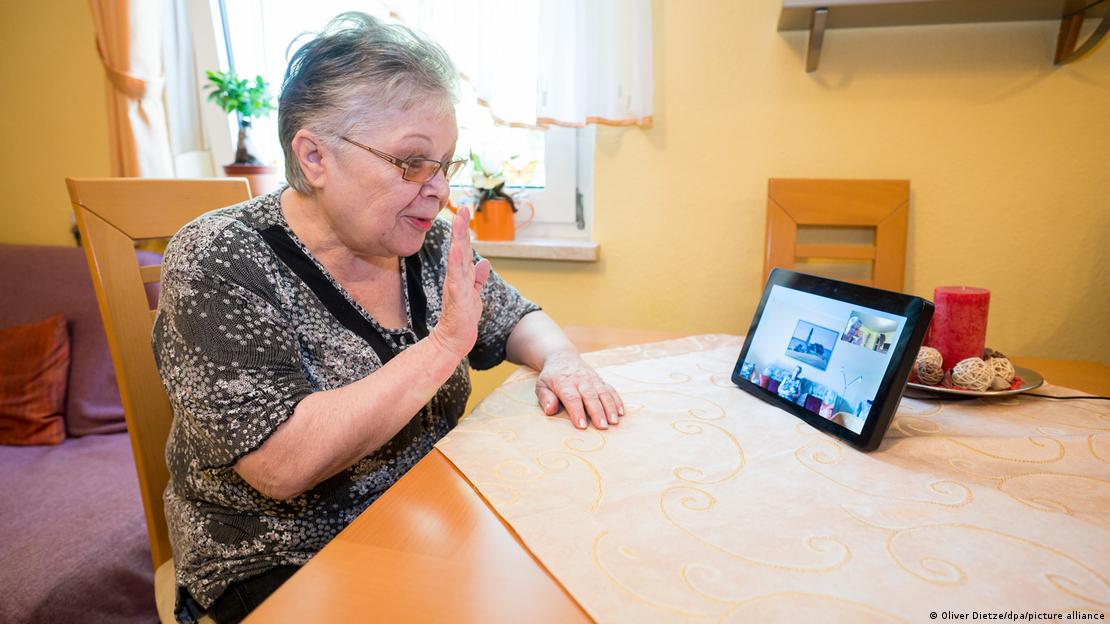 Yaşlı bir kadın tablet bilgisayardan görüntülü bir görüşme yapıyor ve el sallıyor 