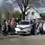 Mehrere Mitglieder der Bürgerenergie Rhein-Sieg eG stehen mit ihren Kindern bei der Einweihung eines Carsahringstandort auf einem Parkplatz vor Elektroautos