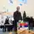 Aleksandar Vucic deposita voto em urna acrílica transparente com bandeira de seu país diante de fotógrafos