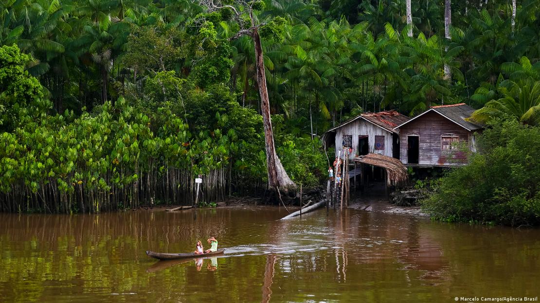 Casas simples de madeira à margem de um rio. Duas crianças em uma canoa