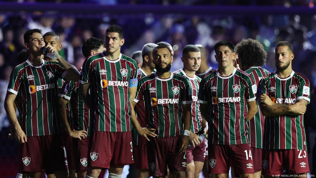 Imagem de cinco jogadores do Fluminense durante jogo, enfileirados um ao lado do outro.