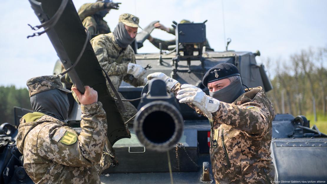 Das Bild zeigt ukrainische Soldaten beim Kampftraining am deutschen Panzer Leopard 1 A5 auf dem Truppenplatz Klietz im Bundesland Sachsen-Anhalt mit frontalem Blick auf das Kanonenrohr von dem rechts und links ukrainische Soldaten die Rohrabedeckung entfernen.  