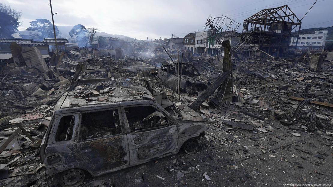 Un vehículo completamente calcinado junto a varias casas destruídas por el fuego.