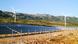 Two rows of solar panels can be seen between a fence and two wind turbines. There are mountains in the background. Zadar, southern Croatia Two rows of solar panels can be seen between a fence and two wind turbines. There are mountains in the background. Zadar, southern Croatia