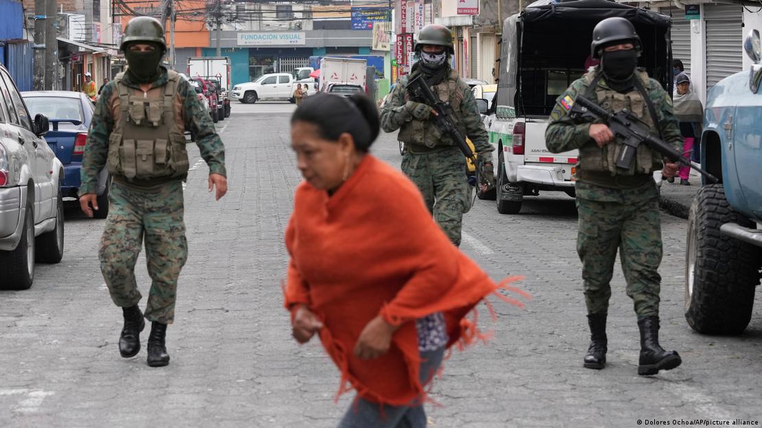 Mulher atravessa a rua diante de três militares armados