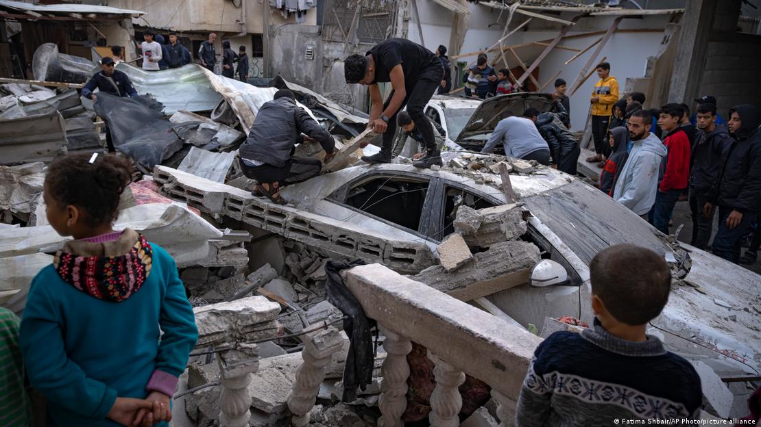 Palestinezët shohin e kërkojnë në një ndërtesë pas bombardimit në Rafah, shkatërrim, copa betoni të rënda, makina e goditur nga copat e betonit të rëna nga lart