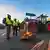 Deutschland | Bauernproteste. Landwirte blockieren mit ihren Traktoren eine Autobahnauffahrt nach Berlin. Im Vordergrund ist eine Feuerschale zu sehen, in der Holz brennt. Davor stehen Bauern in gelben Warnwesten. Foto vom 8. Januar. 