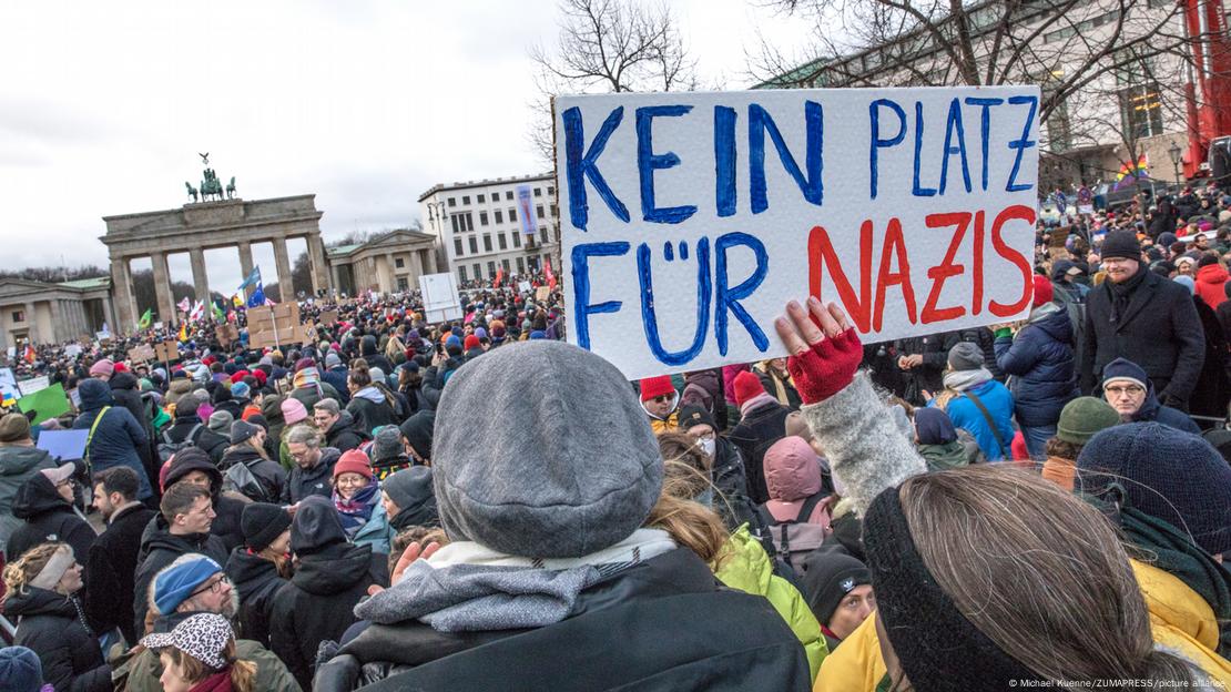 Multidão em frente ao Portão de Brandemburgo. Em primeiro plano, uma pessoa ergue placa onde se lê "kein platz für Nazis".