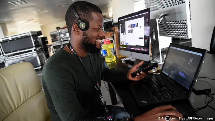 A journalist wearning headphones sits in front of a laptop with a monitor next to him as he searches the internet at the Arise News in Lagos in 2021. 