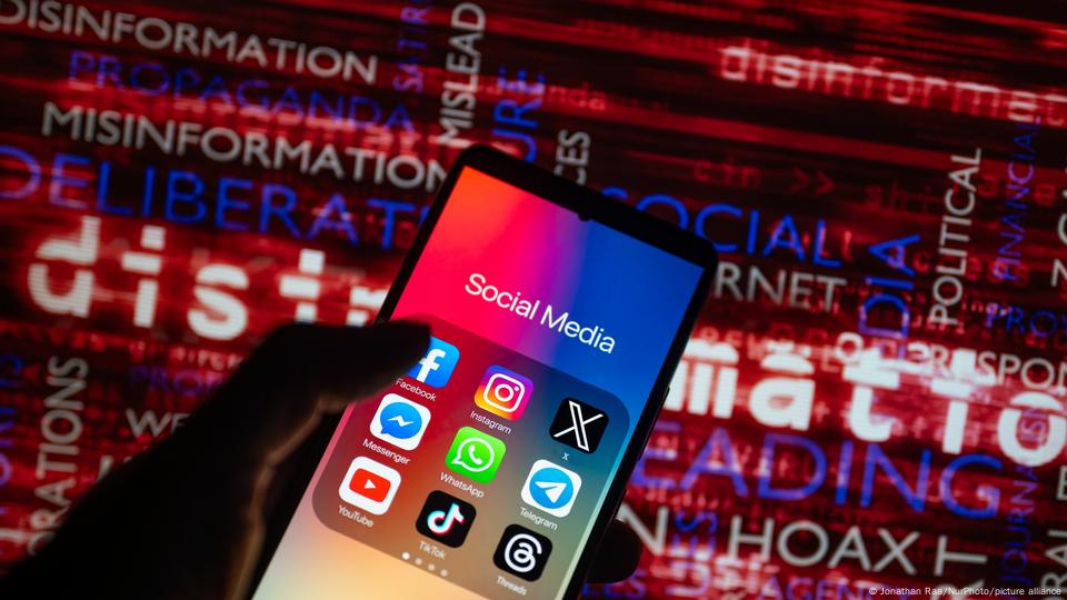 Social media icons are seen on a smartphone screen with words such as 'disinformation', 'misinformation' and 'hoax' on a screen the background