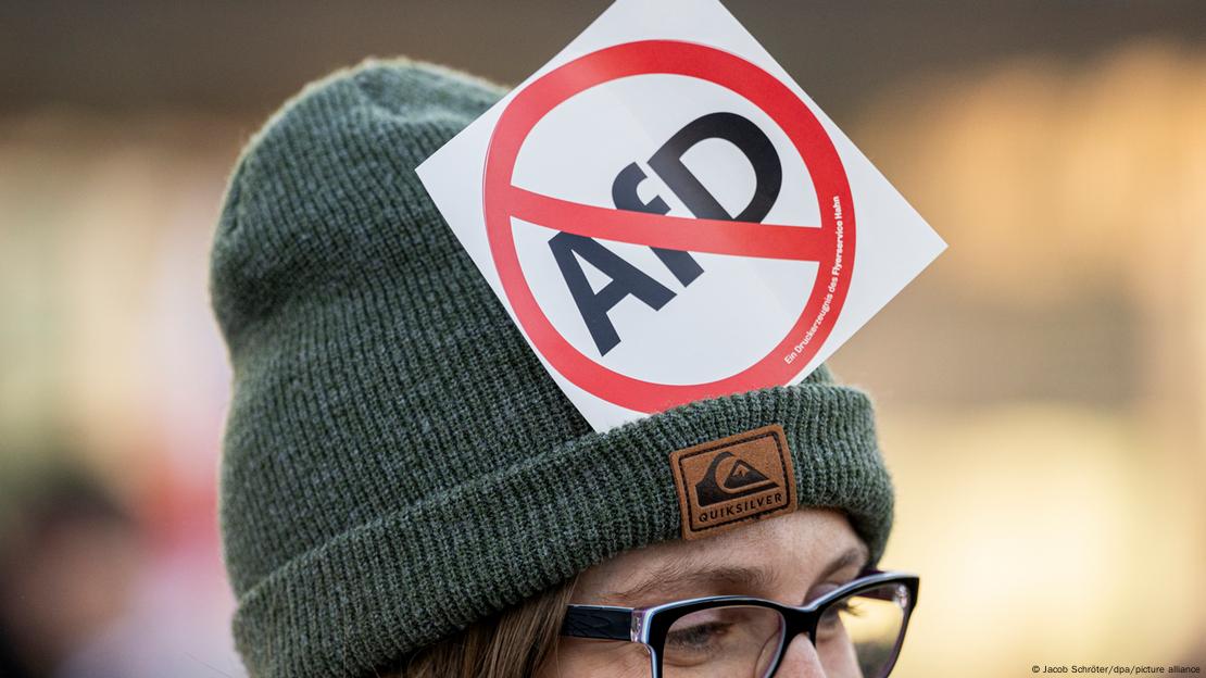 A person wearing a hat with a sticker of an AfD in a red circle with a line though it