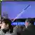 People watch a television screen showing a news broadcast with file footage of a North Korean missile test, at a railway station in Seoul on January 24, 2024..