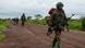 A man armed with an assault rifle and wearing military uniform walks ahead of three others along a dirt road A man armed with an assault rifle and wearing military uniform walks ahead of three others along a dirt road