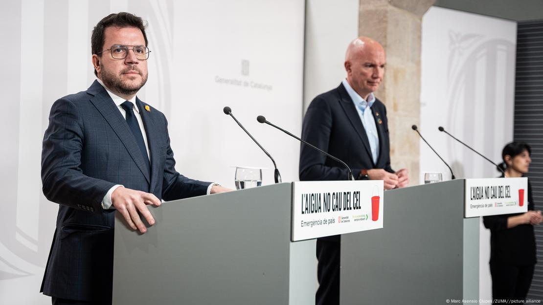 Dos hombres de traje ante dos micrófonos, dando una rueda de prensa.