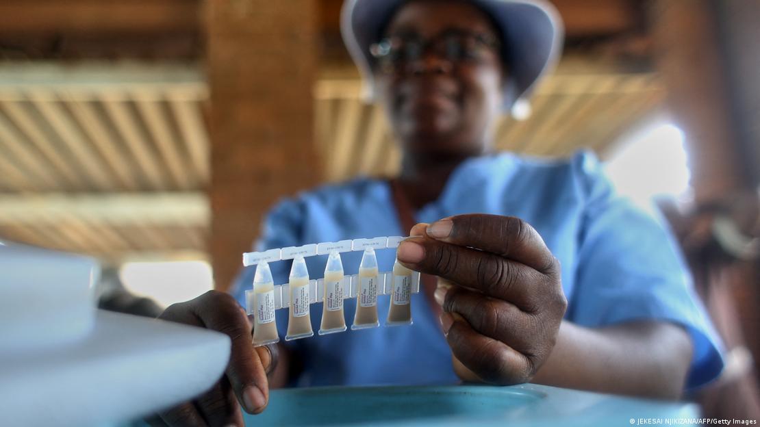 A woman, blurry in the background, holds up five little vials of cholera vaccines A woman, blurry in the background, holds up five little vials of cholera vaccines