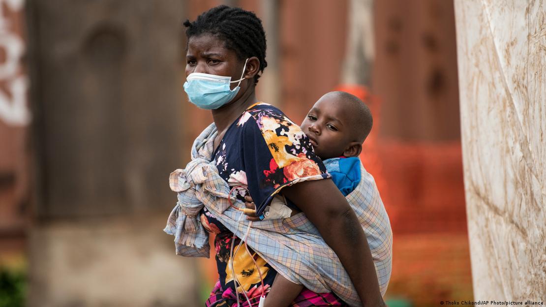 A woman wearing a face mask is carrying her ill son on her back A woman wearing a face mask is carrying her ill son on her back