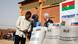 Two Burkina Faso government members and the Russian ambassador are talking behind bags of grain carrying the flags of both countries