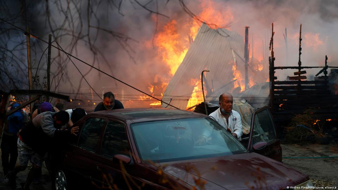 Homens empurrando um carro com edifício em chamas atrás