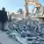 Männer stehen auf den Trümmern des Hauptquartiers der Hashd al-Shaabi, ein Bagger räumt den Schutt weg 