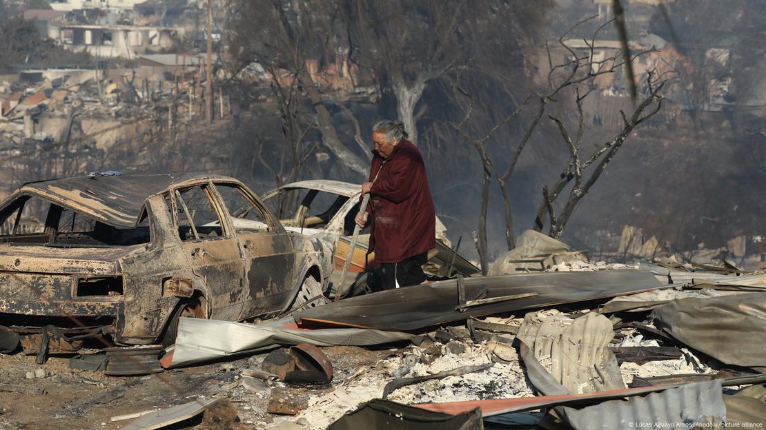 Idosa caminha entre carros queimados e casas destruidas por incêndio no Chile