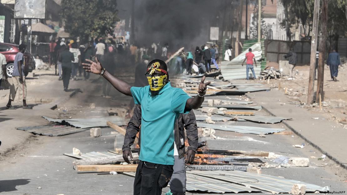 Des manifestants, en février 2023, qui protestent à Dakar contre le report de la présidentielle. On voit des débris qui jonchent la rue, un manifestants masqué les bras en l'air et de la fumée derrière lui (archive) Des manifestants, en février 2023, qui protestent à Dakar contre le report de la présidentielle. On voit des débris qui jonchent la rue, un manifestants masqué les bras en l'air et de la fumée derrière lui (archive)