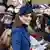 The Princess of Wales, wearing a blue hat, smiles in front of a crowd taking photos