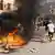 Des personnes courent dans une rue de Dakar où un feu brûle au milieu de la chaussée (photo du 9 février 2024)