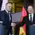 Donald Tusk, left, shaking hands with Olaf Scholz at a press conference. They are smiling and facing the cameras, in front of Polish, German and EU flags.