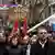 Männer und Frauen protestieren gegen die kosovarische Regierung mit Fahnen und einem Pappschild