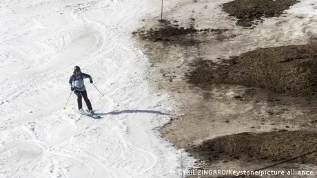 Eine Person fährt Ski auf einer Schneepiste; auf der rechten Bildhälfte ist der Boden schneefrei.