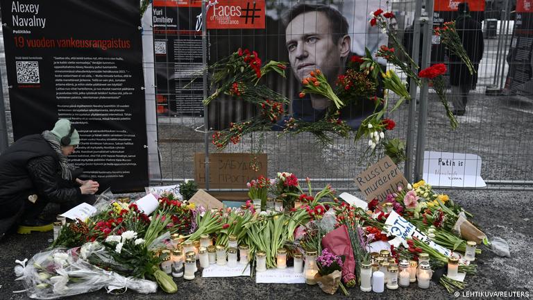 Foto de una persona que coloca flores cerca de una pancarta con la cara de Navalny.