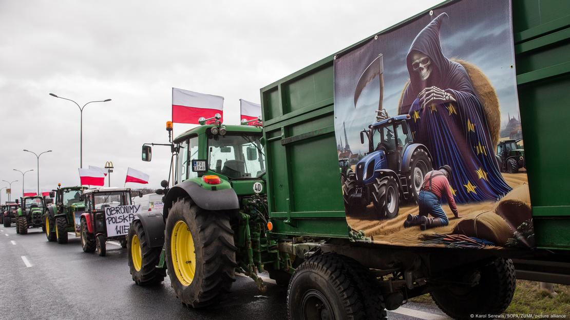 Polen Bauernproteste: Auf einem Traktoanhänger ist ein Bild zu sehen: Der Sensenmann im EU-Gewand hinter einem Traktor, daneben kniet geschlagen der Bauer