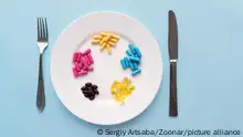 Colorful pills in a large white bowl along with a fork and knife on a blue background. Health concept