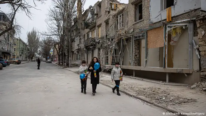 A family in Kherson walks down a heavily damaged street.